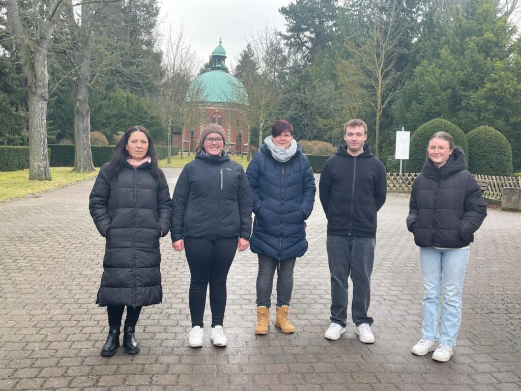 Eine Gruppe von fünf Menschen vor einem Friedhof