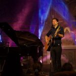 Portrait des Künstlers Lennert Schilgen mit Gitarre in bunt beleuchteter Kirche